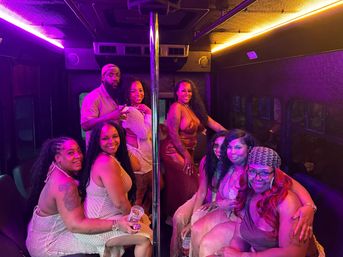 Smiling group of friends inside a neon-lit party bus gathered around a chrome dance pole, wearing colorful party outfits and holding drinks.