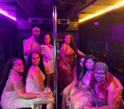 Smiling group of friends inside a neon-lit party bus gathered around a chrome dance pole, wearing colorful party outfits and holding drinks.