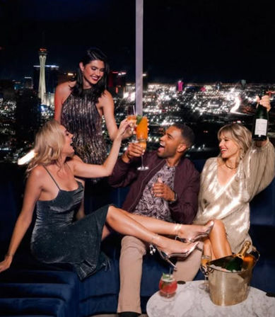 Friends celebrating with cocktails and champagne on a rooftop lounge overlooking the Las Vegas skyline at night