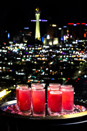 Tray of pink cocktails in tall glasses on ice with neon-lit Las Vegas skyline and Stratosphere Tower bokeh at night