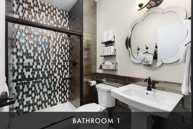 Contemporary bathroom with hexagon mosaic shower tiles behind a glass sliding door, metallic subway tile accent, white pedestal sink and toilet, and scalloped decorative mirror.