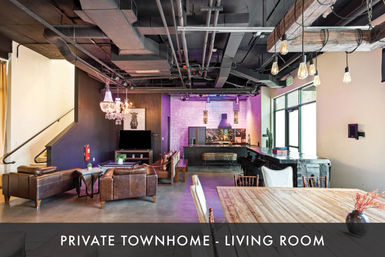 Industrial-chic townhome living room with exposed ductwork and Edison pendants, leather sofas around a coffee table, crystal chandelier, wall TV, open kitchen and bar with purple accent lighting, and a large wooden dining table.