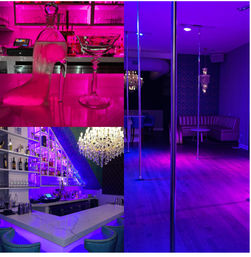 Neon-lit urban nightclub interior with a martini glass and shoe-shaped decanter on a marble bar, illuminated liquor shelves and crystal chandelier, plus dance poles and leather banquette seating bathed in pink and purple lighting.