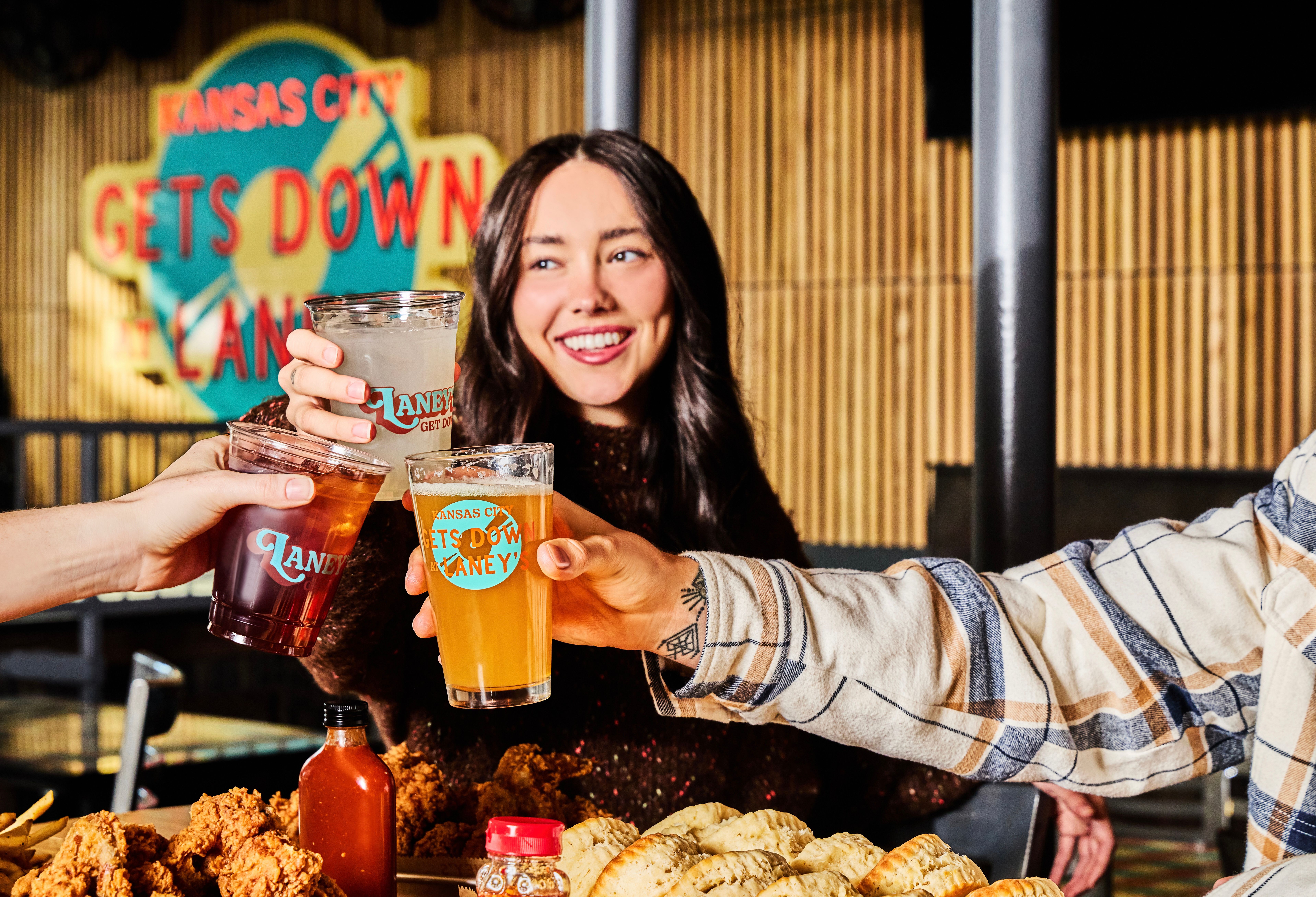 Friends cheerfully toasting with beers and cocktails over fried chicken and biscuits at a lively Kansas City eatery