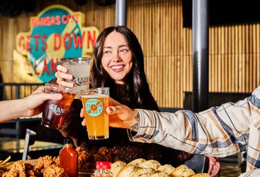 Friends cheerfully toasting with beers and cocktails over fried chicken and biscuits at a lively Kansas City eatery