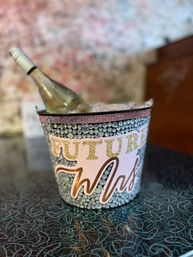 Rhinestone-decorated ice bucket labeled "Future Mrs." holding a chilled white wine bottle on a retro patterned countertop, bachelorette party vibe
