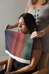 Stylist holds a striped color drape against a seated client's neckline for personal color analysis and wardrobe styling in a studio.