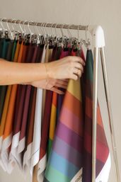 Hands browsing colorful fabric swatches clipped on a chrome garment rack, showing striped and solid textile color samples.