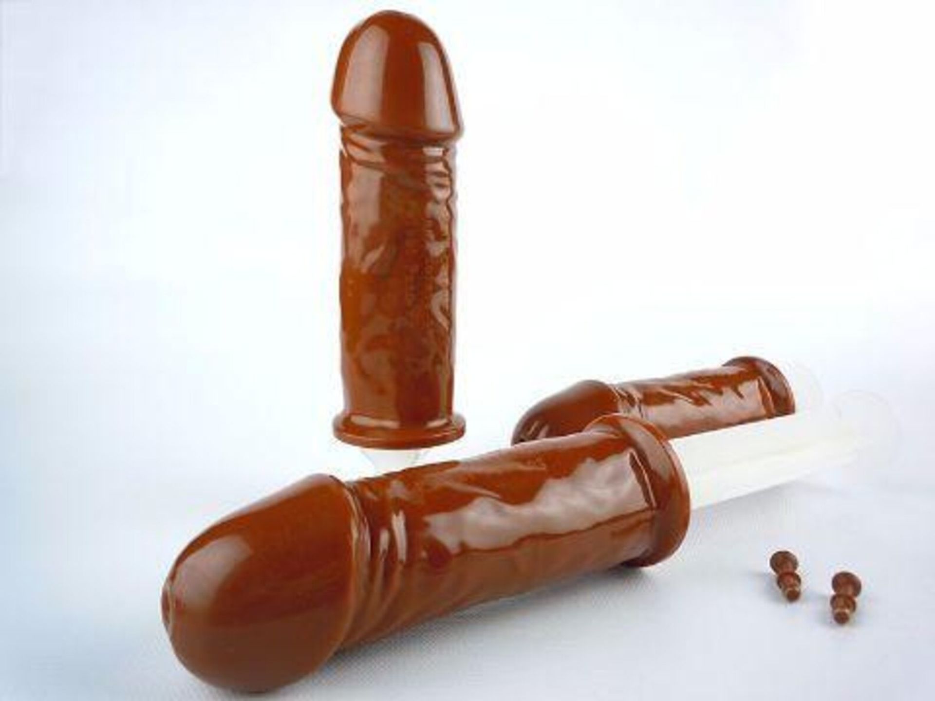 Three penis-shaped chocolate popsicles and silicone molds on a white background, novelty adult dessert treat