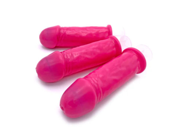 Three bright pink novelty penis-shaped ice pop molds with suction cups on a white background