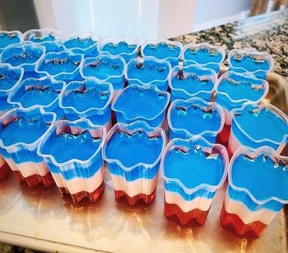 Rows of red, white and blue layered gelatin cups in flower-shaped clear molds on a kitchen counter, festive patriotic dessert for Fourth of July