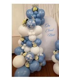 Cloud-themed blue and white balloon garland with marbled cloud balloons and baby's-breath and cream hydrangea accents beside an 'On Cloud Nine' backdrop on a wooden floor.