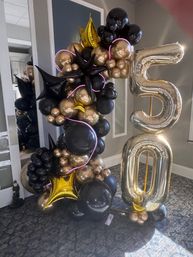 Black and metallic gold balloon garland with star-shaped accents and pink LED trim, paired with large gold foil '5' and '0' number balloons for a 50th indoor celebration