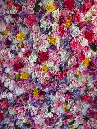 Vibrant floral wall backdrop with densely packed pink, purple, white and yellow roses, peonies and mixed blossoms — close-up decorative texture for events and photos