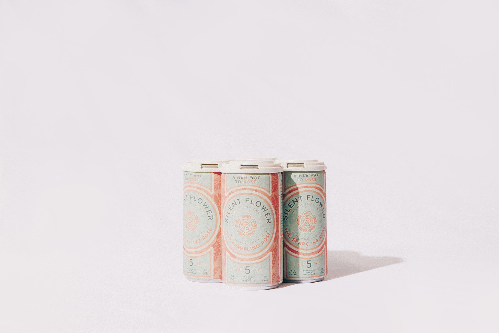 Three pastel-labeled sparkling rosé cans grouped on a clean white background, soft mint and coral design with visible pull-tab tops — minimalist beverage product shot.