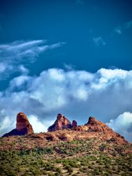 Sunlit red‑rock buttes rising above green desert scrub in the American Southwest under a deep blue sky with billowing white clouds