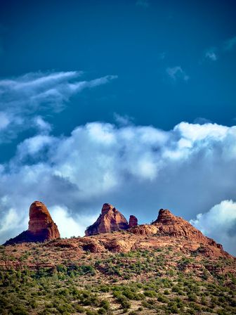 Sunlit red‑rock buttes rising above green desert scrub in the American Southwest under a deep blue sky with billowing white clouds