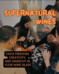 Playful wine-tasting at an art event: people gathered around a decorated table, sipping wine and sorting sticker cards beneath bold orange promotional text.