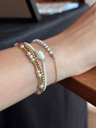 Close-up of wrist wearing a stacked, beachy bracelet set with gold and pearl beads, white shell charm, tiny white seed beads and a delicate gold chain.