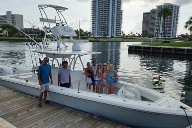 Group of people posing on a center-console fishing boat docked at a waterfront marina with high-rise condo towers in the background