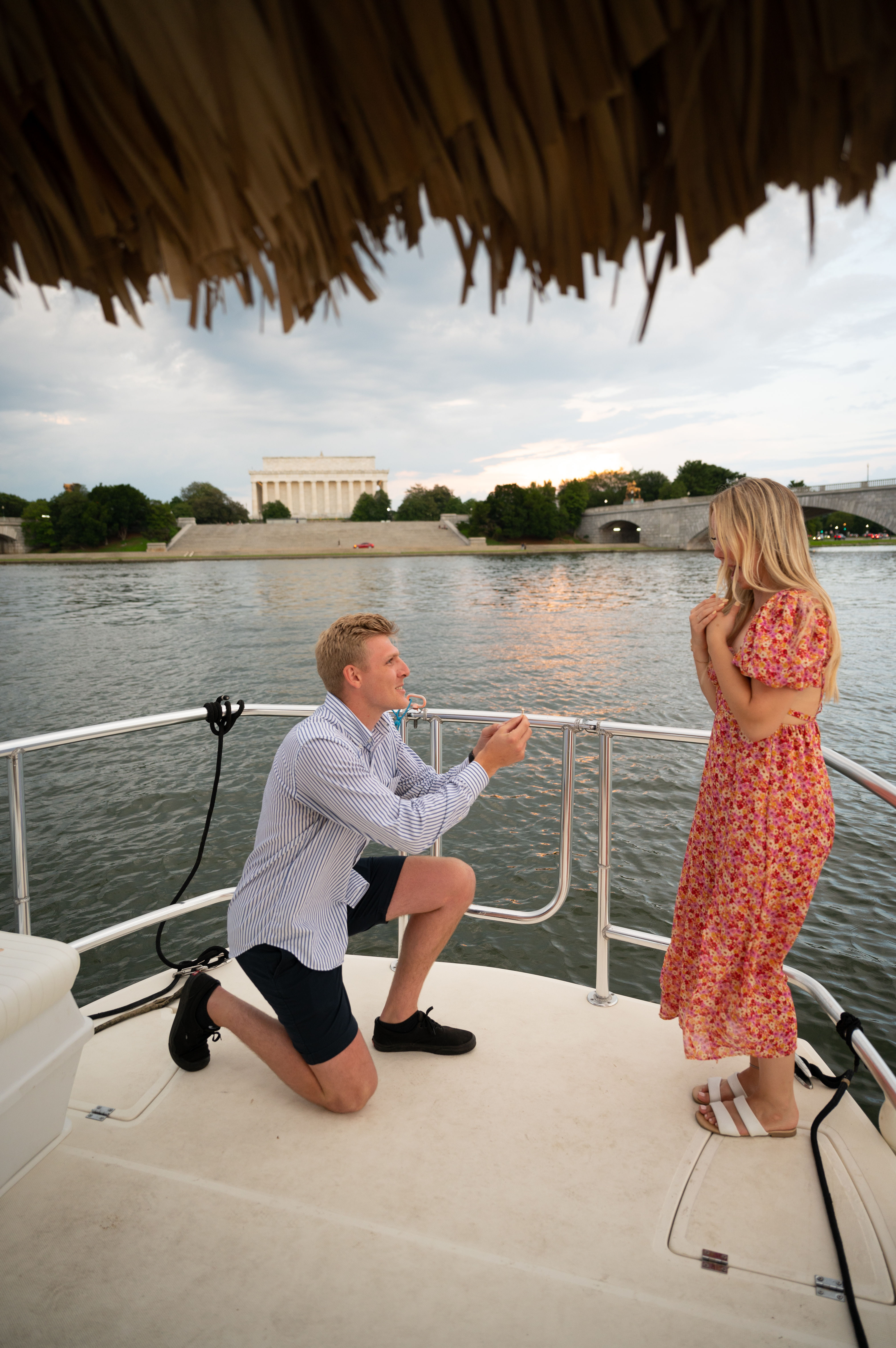 Man kneeling to propose to woman on a boat at sunset, Lincoln Memorial and Memorial Bridge across the Potomac River in Washington, D.C.