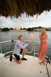 Man kneeling to propose to woman on a boat at sunset, Lincoln Memorial and Memorial Bridge across the Potomac River in Washington, D.C.