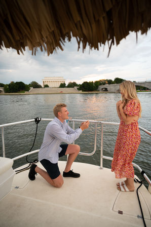 Man kneeling to propose to woman on a boat at sunset, Lincoln Memorial and Memorial Bridge across the Potomac River in Washington, D.C.
