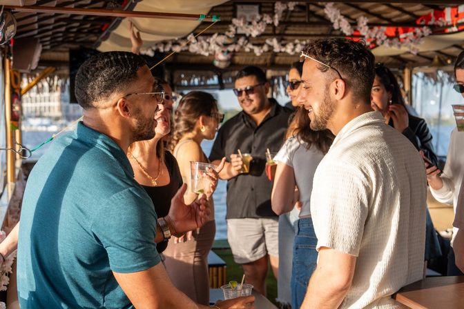 Smiling group of friends enjoying cocktails and conversation on a sunny waterfront boat near a marina, casual summer outfits and festive decorations