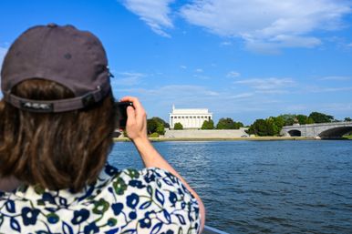 Visitor photographing the Lincoln Memorial and Arlington Memorial Bridge across the Potomac River on a sunny blue-sky day