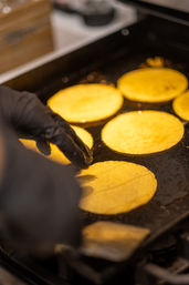 Gloved hand flipping golden corn tortillas sizzling on a hot flat-top griddle in a commercial kitchen