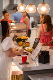 Casual indoor party: guests serving themselves at a kitchen island buffet with chips, dips, lime wedges and glowing pendant lights.