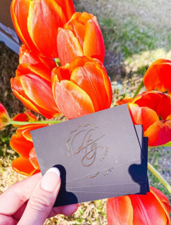 Close-up of vibrant red-orange tulips in a sunny garden, with a hand holding black embossed business cards.