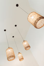 Four woven rattan pendant lights with warm glowing bulbs hanging from a white ceiling, modern boho indoor lighting.