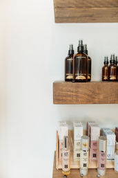 Amber oil spray bottles and skincare serums arranged on rustic wooden shelves against a white wall in a minimalist boutique spa display