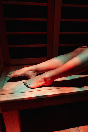 Bare legs and feet resting on a wooden sauna bench, bathed in moody red and green light