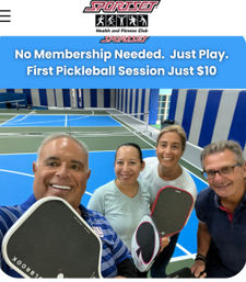Smiling group selfie of four adults holding pickleball paddles on an indoor blue-and-green pickleball court beneath a banner promoting no-membership beginner pickleball sessions.