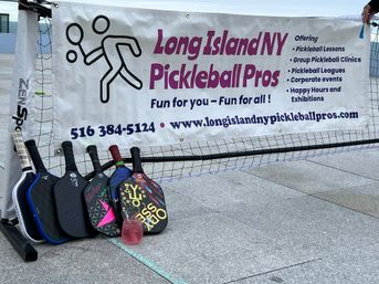 Outdoor Long Island, NY pickleball setup on a city plaza with a promotional banner, net and five colorful paddles lined up