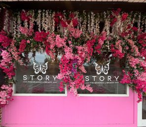 Pink storefront with cascading pink and white flowers framing a boutique fragrance shop window and decorative butterfly logos on the glass