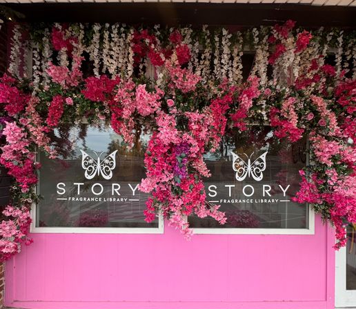 Pink storefront with cascading pink and white flowers framing a boutique fragrance shop window and decorative butterfly logos on the glass