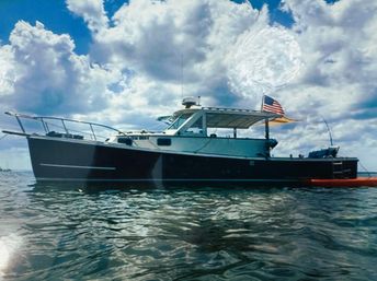 Sleek motor yacht with shaded cockpit and American flag anchored on shimmering coastal waters beneath dramatic billowy clouds, orange kayak tied alongside.