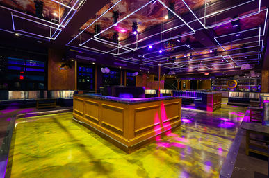 Modern nightclub interior with glowing yellow-green dance floor, central wooden bar, purple neon grid ceiling lights, and plush lounge seating