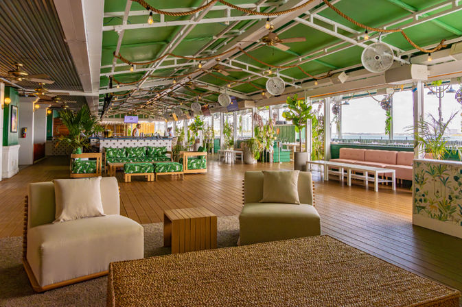 Rooftop lounge and outdoor bar with green ceiling, wooden deck, tropical plants, cushioned seating, ceiling fans and waterfront view