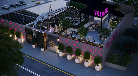 Aerial view of an urban rooftop lounge at dusk with a glass dome, neon pink signage, cozy outdoor seating, potted trees in oversized planters along the sidewalk, and a nearby parking area.