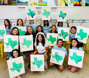 Smiling paint-party group in an art studio holding canvases of green Texas map paintings decorated with flowers and doodles, bride-to-be wearing a veil seated in the center.