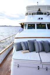 Luxury yacht deck with white quilted sunbed, grey striped cushions and a small beige clutch on teak decking, overlooking calm ocean waters