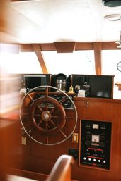 Sunlit boat helm with a polished wooden ship wheel and vintage marine control panel inside a classic nautical cabin.