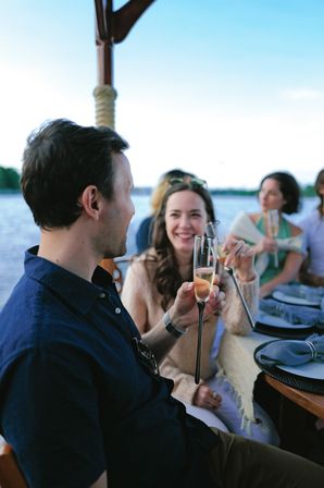 Cheerful friends clinking champagne flutes on a boat over calm lake waters during a relaxed outdoor dinner cruise