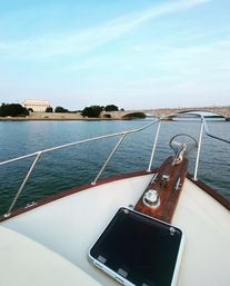 Bow of a boat on the Potomac River in Washington, D.C., heading toward Arlington Memorial Bridge with the Lincoln Memorial and Washington Monument on the horizon under a pale blue sky