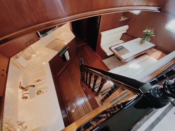 Wood-paneled yacht interior seen from stairs: glossy black railing, compact galley with sink and stove, and white-leather dinette with vase of flowers.