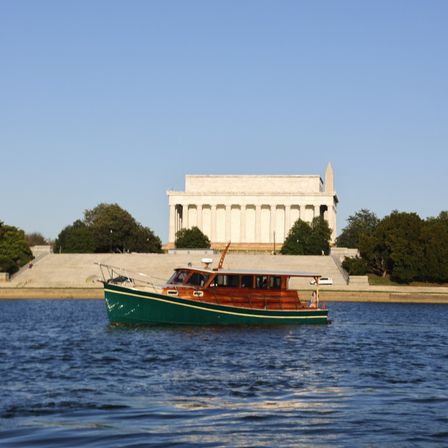 Green-and-wood cabin boat skimming the water in front of the Lincoln Memorial and Washington Monument on a sunny day in Washington, D.C.